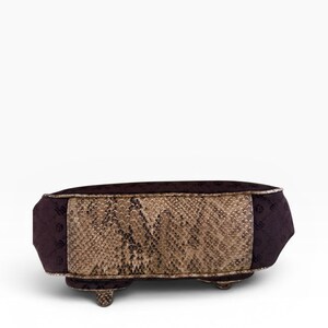 May include: A rectangular handbag with a snakeskin pattern on the front and sides. The bag has a dark purple fabric on the top and ends, with small feet. The bag is a neutral colour.
