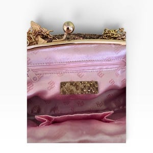 May include: A pink satin handbag with a gold clasp and chain. The interior has a pink lining with a repeating pattern and a small pocket. A gold rectangular label is visible inside the bag.