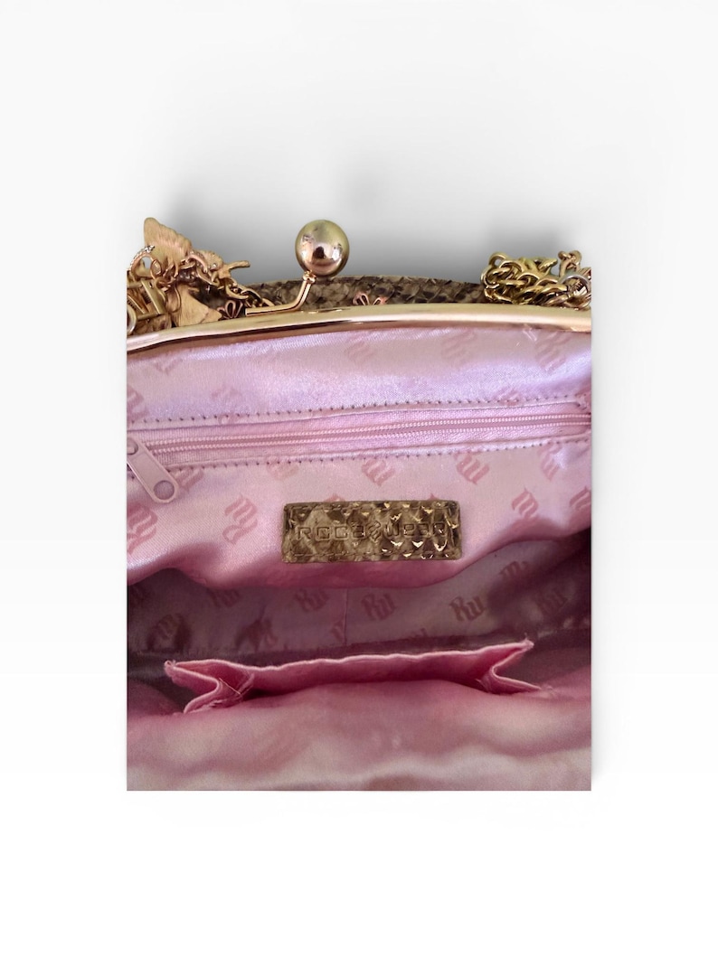 May include: A pink satin handbag with a gold clasp and chain. The interior has a pink lining with a repeating pattern and a small pocket. A gold rectangular label is visible inside the bag.