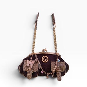 Könnte beinhalten: Dunkelbraune Handtasche mit Kussverschluss, goldfarbenen Kettenriemen und zwei kleinen Taschen. Die Tasche hat eine Schmetterlingsverzierung und eine dekorative Kette mit kleinen Schmetterlingsanhängern. Die Tasche hat ein braunes Schlangenhautmuster.