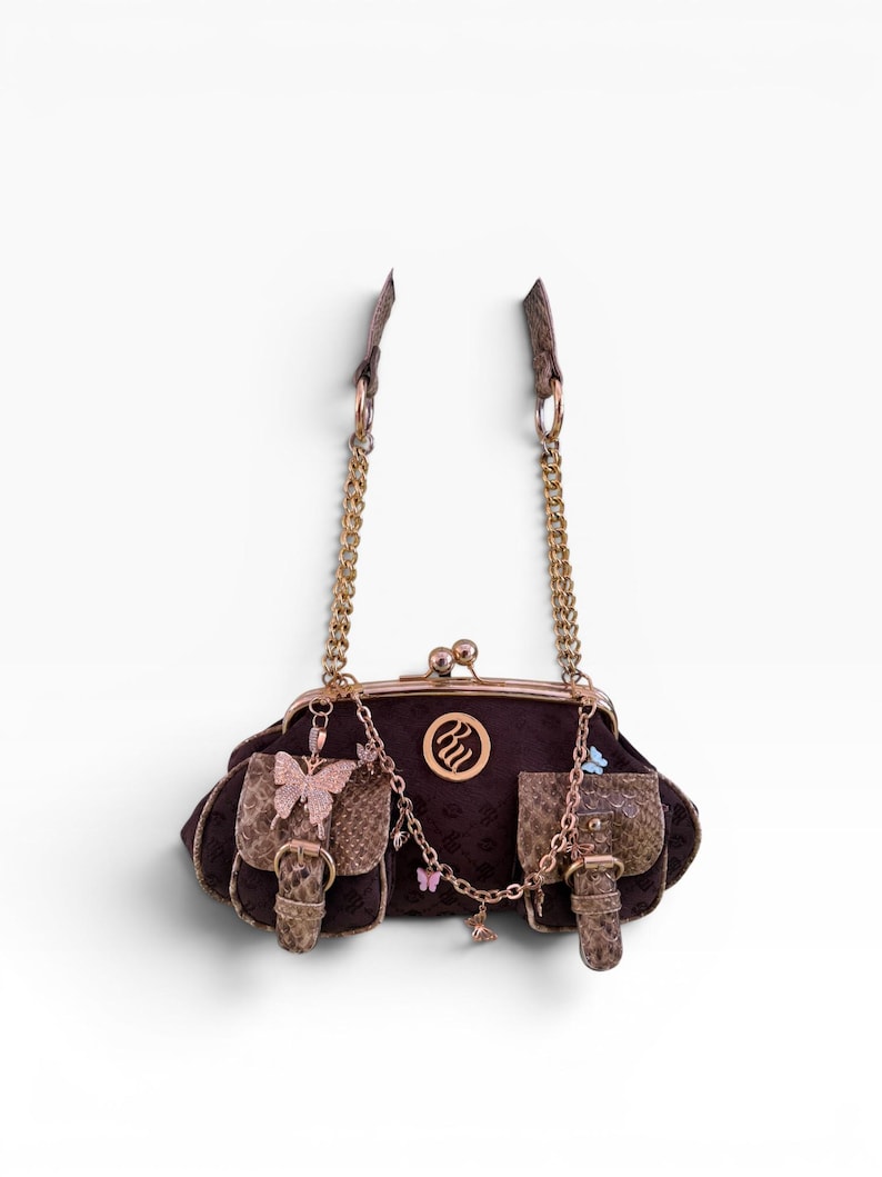 May include: A dark brown handbag with a kiss-lock clasp, gold chain straps, and two small pockets. The bag features a butterfly embellishment and a decorative chain with small butterfly charms. The bag has a brown snakeskin pattern.