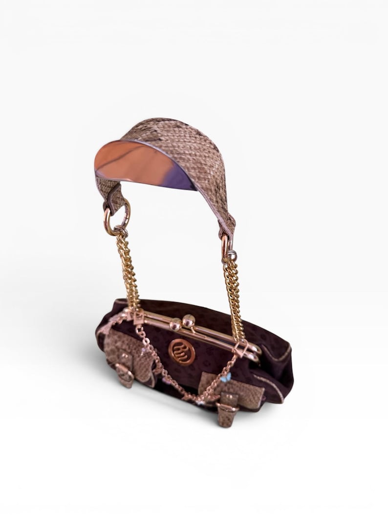 May include: A dark brown handbag with a gold chain strap and a woven visor-like handle. The bag features gold hardware and decorative accents. The bag is approximately 20 cm long.