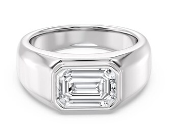 May include: A polished silver ring with a rectangular, emerald-cut gemstone. The ring has a wide band and a bezel setting that securely holds the clear, sparkling stone. The design is simple and elegant.