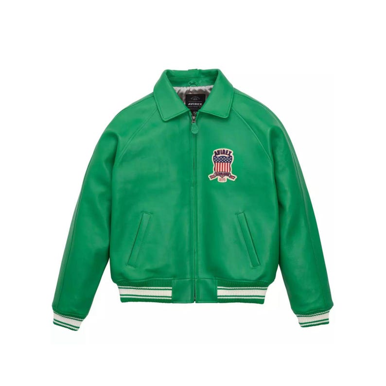 Pu&ograve; includere: Giacca in pelle verde brillante con chiusura a zip e colletto. Presenta una toppa sul petto con un disegno della bandiera americana e la scritta "AVIREX". I polsini e l'orlo sono rifiniti con dettagli a righe bianche e verdi.