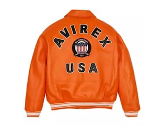 La chaqueta bomber de cuero naranja AVIREX USA Edition ofrece una audaz fusión del estilo aeronáutico clásico y el toque urbano contemporáneo.