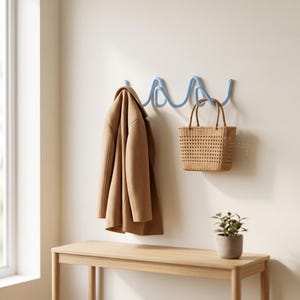 Könnte beinhalten: Eine hellblaue Wandgarderobe mit einem wellenförmigen, durchgehenden Design. Ein beigefarbener Mantel hängt auf der linken Seite und eine geflochtene, beigefarbene Handtasche mit zwei Henkeln hängt auf der rechten Seite der an der Wand befestigten Leiste.