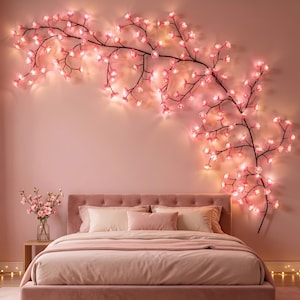May include: A wall-mounted decorative branch light featuring numerous small, glowing pink cherry blossom flowers. The dark, slender branches are arranged in a sprawling, organic pattern across the wall above a bed with pink bedding.