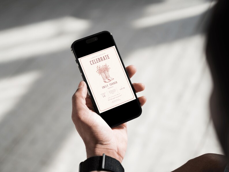 K&ouml;nnte beinhalten: Ein schwarzes Smartphone, das eine digitale Einladung auf seinem Bildschirm anzeigt. Die Einladung zeigt das Wort CELEBRATE in einer Serifenschrift, eine Strichzeichnung von Cowboystiefeln mit Blumen und den Namen EMILY THARIN auf hellem Grund.