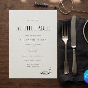 Könnte beinhalten: Eine weiße, rechteckige Einladungskarte mit schwarzem Text, der AT THE TABLE, THE HARRIS DINNER und Veranstaltungsdetails zeigt. Daneben liegen eine dunkelgraue Leinen-Serviette, eine silberne Gabel, ein silbernes Messer und ein kleiner schwarzer Teller.