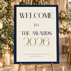 May include: A rectangular event sign with a dark navy blue border and a cream background. The text reads WELCOME TO THE AWARDS 2026 in navy blue and gold, followed by the smaller text An evening of recognition, inspiration and shared success.
