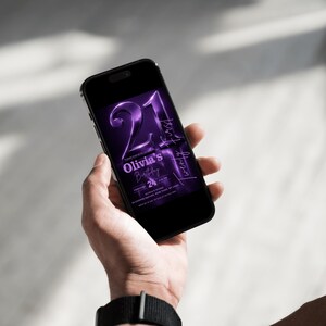 May include: A black smartphone displays a purple digital invitation for "Olivia's Birthday." The invitation features the number "21" in a bold, metallic font, with additional text indicating the date and time of the event. The phone is held in a person's hand.