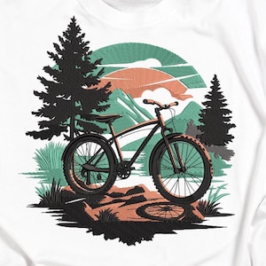 Könnte beinhalten: Ein schwarzes Mountainbike mit orangefarbenen Akzenten ist der Mittelpunkt dieses Designs. Das Fahrrad steht vor einer Bergkulisse mit Bäumen, einem Sonnenuntergang und einem See. Das Design ist auf weißem Hintergrund gestickt.