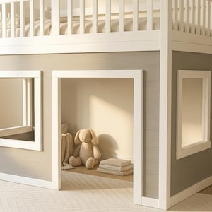 Puede incluir: Una cama alta blanca que cuenta con un área de juego inferior con dos ventanas cuadradas y una entrada central abierta. La estructura tiene una barandilla de seguridad de listones en el nivel superior y paneles de color gris claro en las paredes.