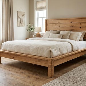 May include: A platform bed frame constructed from light brown wood with a horizontal plank headboard. The bed is dressed with a white fitted sheet, a thick beige duvet, and four rectangular pillows in varying shades of cream and light tan.