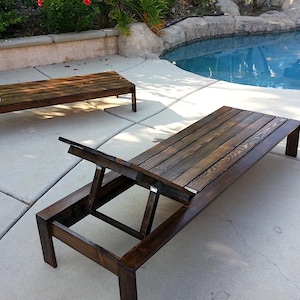 Może przedstawiać: Dwa drewniane leżaki ogrodowe w kolorze ciemnobrązowym z regulowanymi oparciami. Znajdują się na betonowym patio w pobliżu basenu. Oparcia są częściowo podniesione.