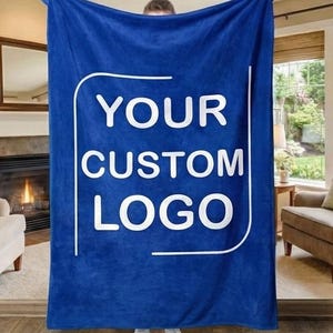 May include: A deep blue blanket displaying the text "YOUR CUSTOM LOGO" in white. The blanket is held up, revealing its size and the custom text. The blanket looks soft and plush, suitable for home decor or personalised gifts.
