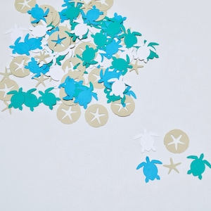 May include: A pile of teal, white, and tan paper cutouts of sea turtles and sand dollars. The cutouts are scattered on a white background.