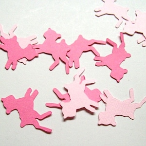 May include: Pink paper cutouts of horses scattered on a white surface. The horses are in various poses and sizes.