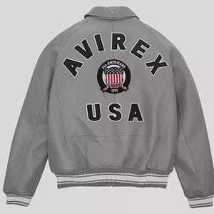 May include: A gray bomber jacket with the word "AVIREX" arched across the back in black letters. Below the word "AVIREX" is a circular patch with the words "ALL AMERICANS" and "ESTABLISHED 1975" surrounding a design of the American flag. The word "USA" is below the patch.