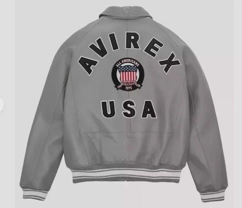 May include: A gray bomber jacket with the word "AVIREX" arched across the back in black letters. Below the word "AVIREX" is a circular patch with the words "ALL AMERICANS" and "ESTABLISHED 1975" surrounding a design of the American flag. The word "USA" is below the patch.