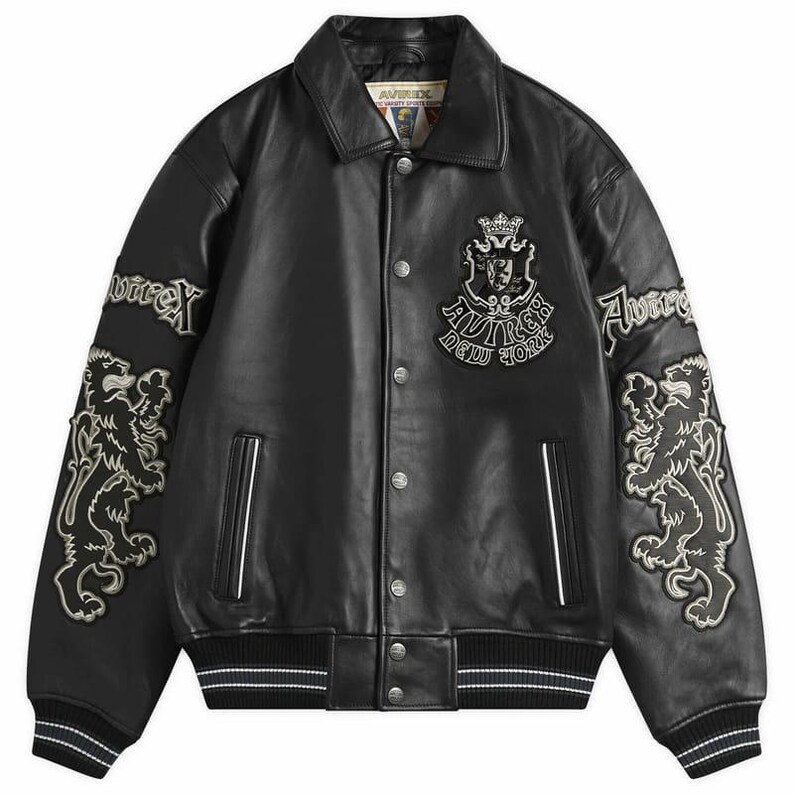 May include: Black leather jacket with a button-up front, embroidered lion and logo patches. The jacket has a classic collar, white stripes on the cuffs and hem, and the brand name "Avirex" is visible.