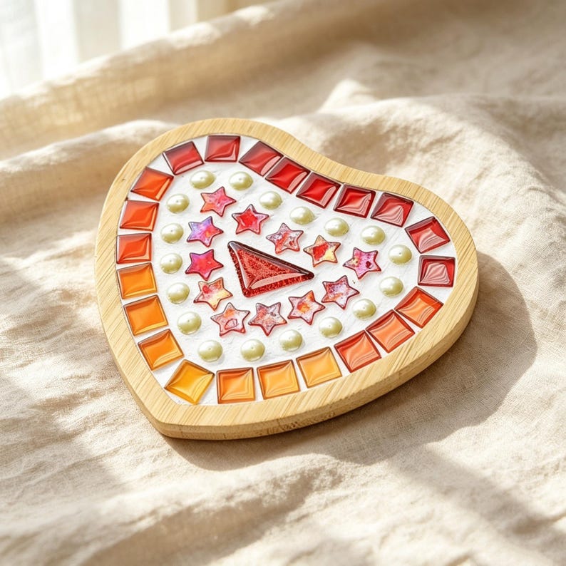 May include: A heart-shaped wooden coaster featuring a mosaic design. The border consists of square red and orange glass tiles. The center is filled with white grout, small iridescent pearl-like beads, red star-shaped glass tiles, and one large red triangular glass piece.