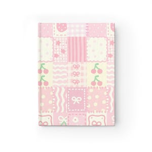 May include: A pink and white journal with a patchwork design. The cover features various patterns including cherries, bows, dots, and stripes. The journal has a rectangular shape and a clean, white background.