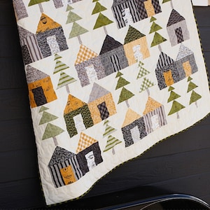 May include: A quilt pattern called "Base Camp" featuring a white background with a repeating pattern of houses and trees in shades of green, black, white, and yellow. The quilt is made with fabric from the "Timer" collection by Sweetwater. The quilt measures 60 inches by 55 inches.