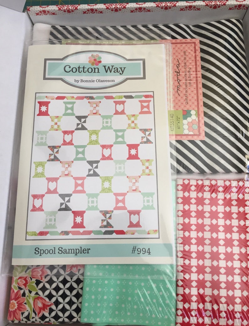 May include: A quilting kit containing fabric and a pattern. The pattern is titled "Spool Sampler" by Bonnie Olaveson. The kit includes various fabrics with floral, geometric, and striped patterns. The kit dimensions are 155cm x 183cm.