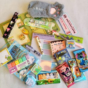 May include: A selection of stationery items with cartoon designs, including pens, notebooks, and sticky notes. The items feature characters like bears, cats, and Stitch. A grey paw-shaped pencil case is also visible, along with a daily planner.