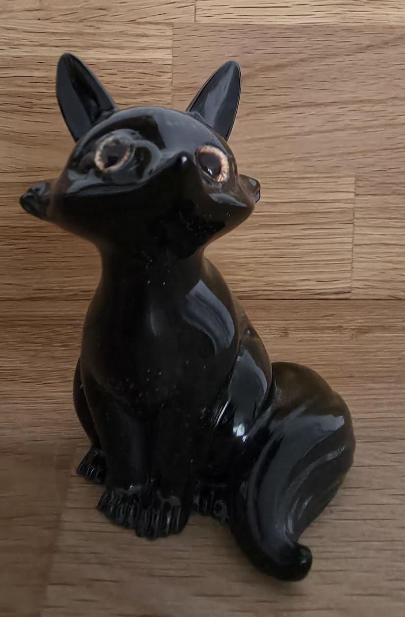 May include: A glossy black fox figurine with pointed ears and a curled tail. The fox is in a seated position, with detailed facial features and light brown eyes. The figurine is a decorative item.
