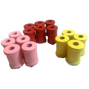 May include: A set of wooden spools in pink, red, and yellow. The spools are all the same size and shape, and they are arranged in a group.