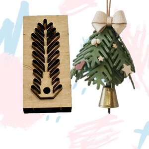 Può includere: Un utensile fustellato in legno con un motivo a foglia e un ornamento decorativo per l'albero di Natale. L'albero è verde con campana dorata, fiocco e stelle. L'ornamento è sospeso da una corda.