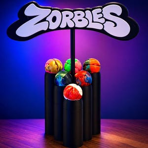 May include: A display featuring the word "ZORBLES" in white lettering on a black sign. Below, six colorful, spherical objects rest on black cylinders. The spheres are various colors, including red, blue, green, and orange.