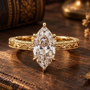 May include: A gold ring featuring a large, clear marquise-cut gemstone held by six prongs. The band is crafted from yellow gold and displays an intricate, engraved scrollwork pattern along its entire outer surface, providing a textured finish.