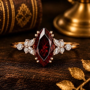 May include: A gold ring featuring a large marquise-cut deep red gemstone at the centre, flanked by clusters of smaller marquise and round-cut clear white stones on each side, set in a polished gold band with a prong setting for each stone.