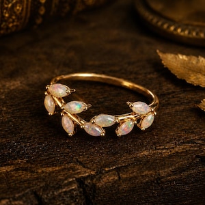 Puede incluir: Un anillo de oro con un delicado diseño de rama adornado con múltiples ópalos de corte marquesa. La banda está hecha de metal dorado pulido y los ópalos muestran destellos de color iridiscentes, dispuestos para parecer hojas en la banda.