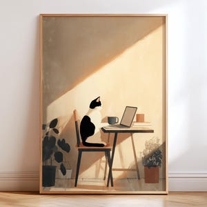 May include: A framed art print depicts a black and white cat seated on a chair at a small table with a laptop, coffee mug, and books. The scene is bathed in warm sunlight, with potted plants adding a touch of greenery. The artwork has a minimalist style.
