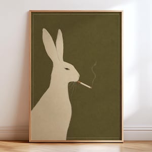 May include: A framed wall art print featuring a cream-colored rabbit in profile against a solid olive green background. The rabbit is depicted with a cigarette in its mouth, from which a thin, light gray wisp of smoke curls upward into the air.