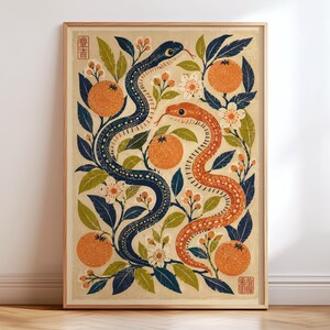 Op de afbeelding: Een rechthoekige wandkunstprint in een houten lijst met een donkerblauwe slang en een oranje slang verstrengeld tussen sinaasappels, groene bladeren en witte bloemen op een beige achtergrond. De print bevat twee rode stempels met tekst.