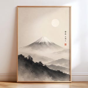 Op de afbeelding: Een ingelijste kunstdruk met een monochroom landschap van een besneeuwde bergtop boven mistige heuvels en donkere, silhouetachtige bomen. Een bleke zon hangt in de lucht, vergezeld door verticale Japanse kalligrafie en een rood zegel.