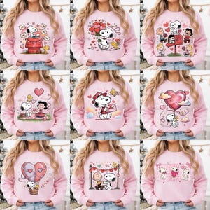 May include: Pink sweatshirts featuring Snoopy and Woodstock in various Valentine's Day designs. Each sweatshirt showcases a different graphic, including Snoopy with hearts, mail, and balloons. The designs are in a cartoon style.