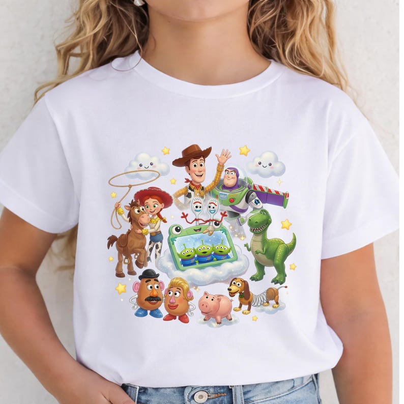 Puede incluir: Una camiseta blanca de manga corta con un estampado gr&aacute;fico colorido de varios personajes animados, incluyendo un vaquero, un guardi&aacute;n espacial, una vaquera, un caballo, un dinosaurio, un perro, un cerdo y varios peque&ntilde;os alien&iacute;genas verdes.