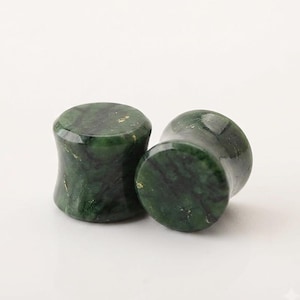 May include: A pair of cylindrical ear plugs with a smooth, polished finish. The plugs feature a deep forest green color with dark, marbled veining throughout the stone surface and subtle flecks of gold-toned inclusions visible on the faces.