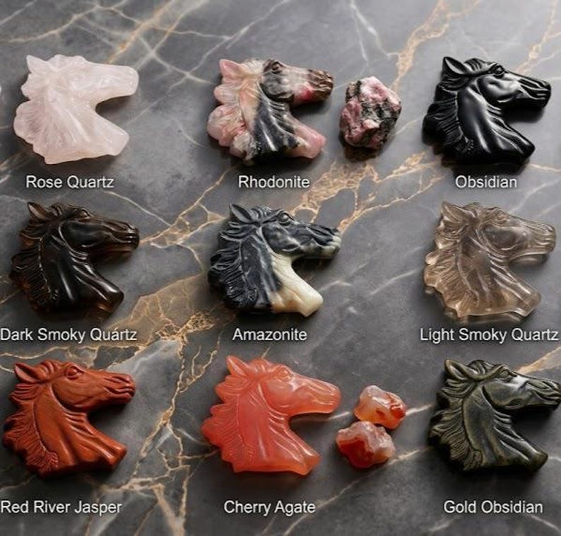 May include: A collection of carved horse head figurines in various gemstones, including rose quartz, obsidian, and cherry agate. The figurines are displayed on a marbled surface, with labels identifying each stone type. The horse heads are detailed and polished.