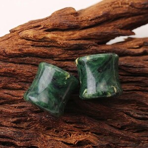 May include: Two cylindrical ear plugs with a smooth, polished finish. The plugs feature a marbled pattern in deep forest green, emerald, and black tones with subtle lighter flecks throughout the material, creating a glossy, stone-like appearance.