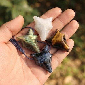 May include: Four fox-shaped pendants carved from various gemstones, including a white stone, a golden-brown tiger's eye, a dark blue-black stone with white inclusions, and a grey-green labradorite with a blue iridescent sheen on a cord.