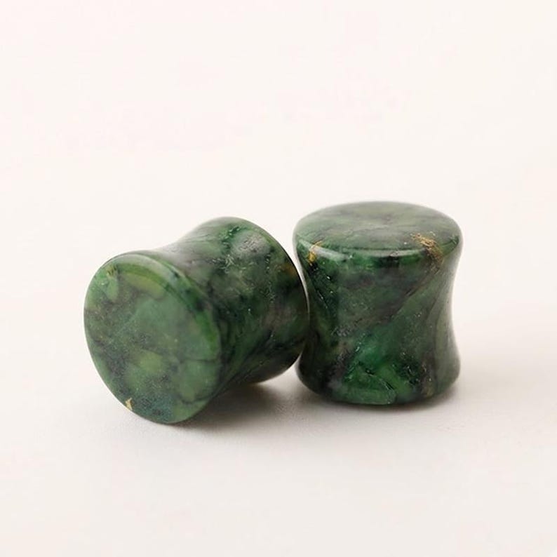 May include: A pair of ear plugs with a concave, saddle-shaped profile. The plugs are crafted from a polished, mottled green stone featuring dark forest green and black veining throughout the surface, creating a natural, marbled appearance.