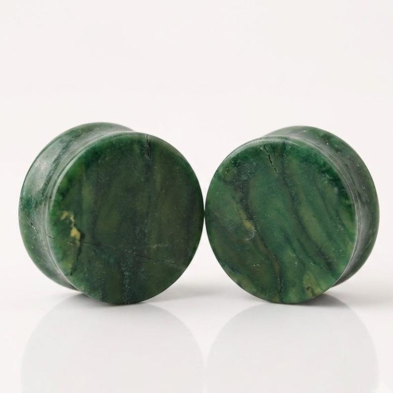 May include: A pair of circular ear plugs crafted from a deep green stone with natural dark veining and mottled patterns. Each plug features a smooth, polished surface with a cylindrical shape, showcasing the unique mineral variations in the stone.