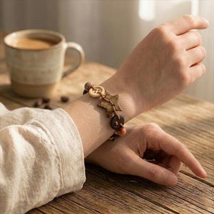 以下が含まれることがあります： 木製のビーズ、ボタン、星型のチャームが付いた手作りのブレスレット。 ブレスレットは茶色のコードに通されており、手首に表示されています。 ユニークなアクセサリーです。